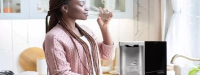 Abertura do post sobre se purificador de água vale a pena: Mulher bebendo água ao lado de purificador